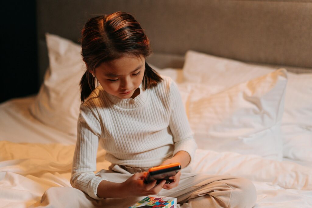 Close-Up Shot of a Girl in White Top Using a Mobile Phone while Sitting on a Bed